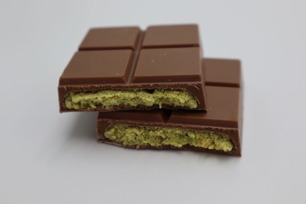 Two pieces of milk chocolate bar stacked and broken open to show a green pistachio filling