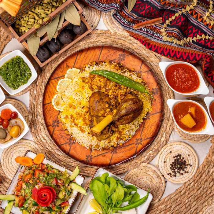 Top view of kabsa on spiced rice surrounded by colourful sauces and fresh vegetables