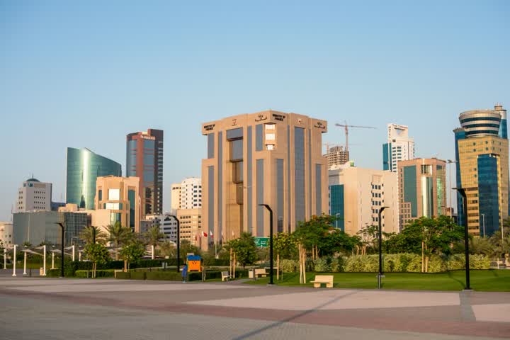 Office towers and a landscaped park with benches and palm trees in Manama’s Diplomatic Area under a clear sky