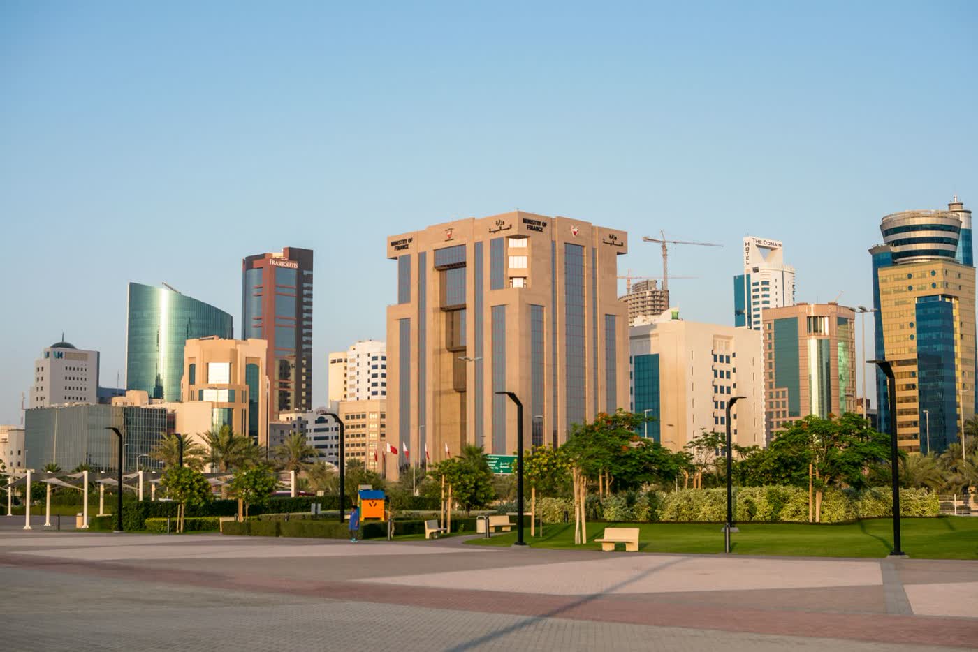 Office towers and a landscaped park with benches and palm trees in Manama’s Diplomatic Area under a clear sky