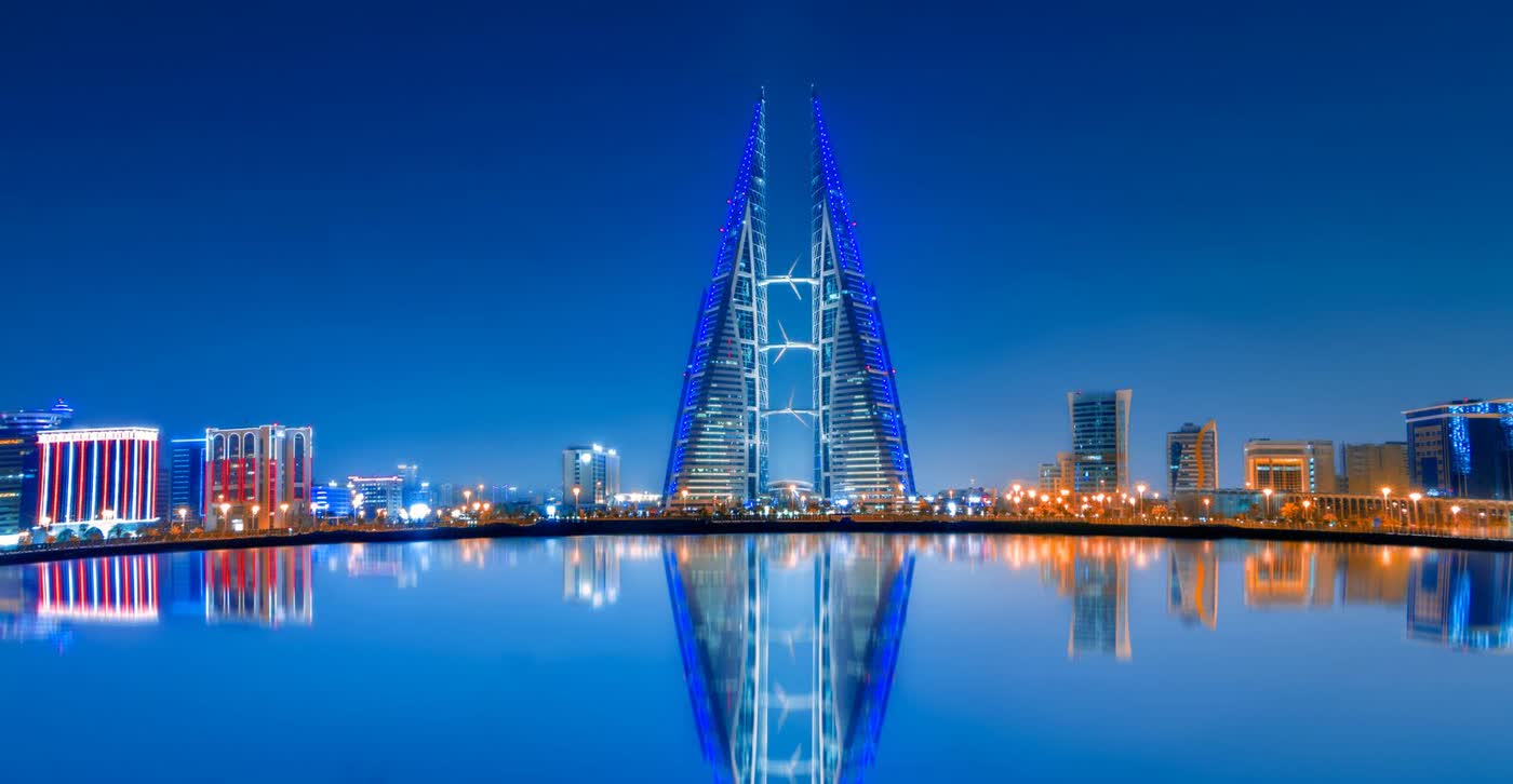 The twin sail-shaped towers of the Bahrain World Trade Center lit in blue at dusk, reflected in a still pool of water