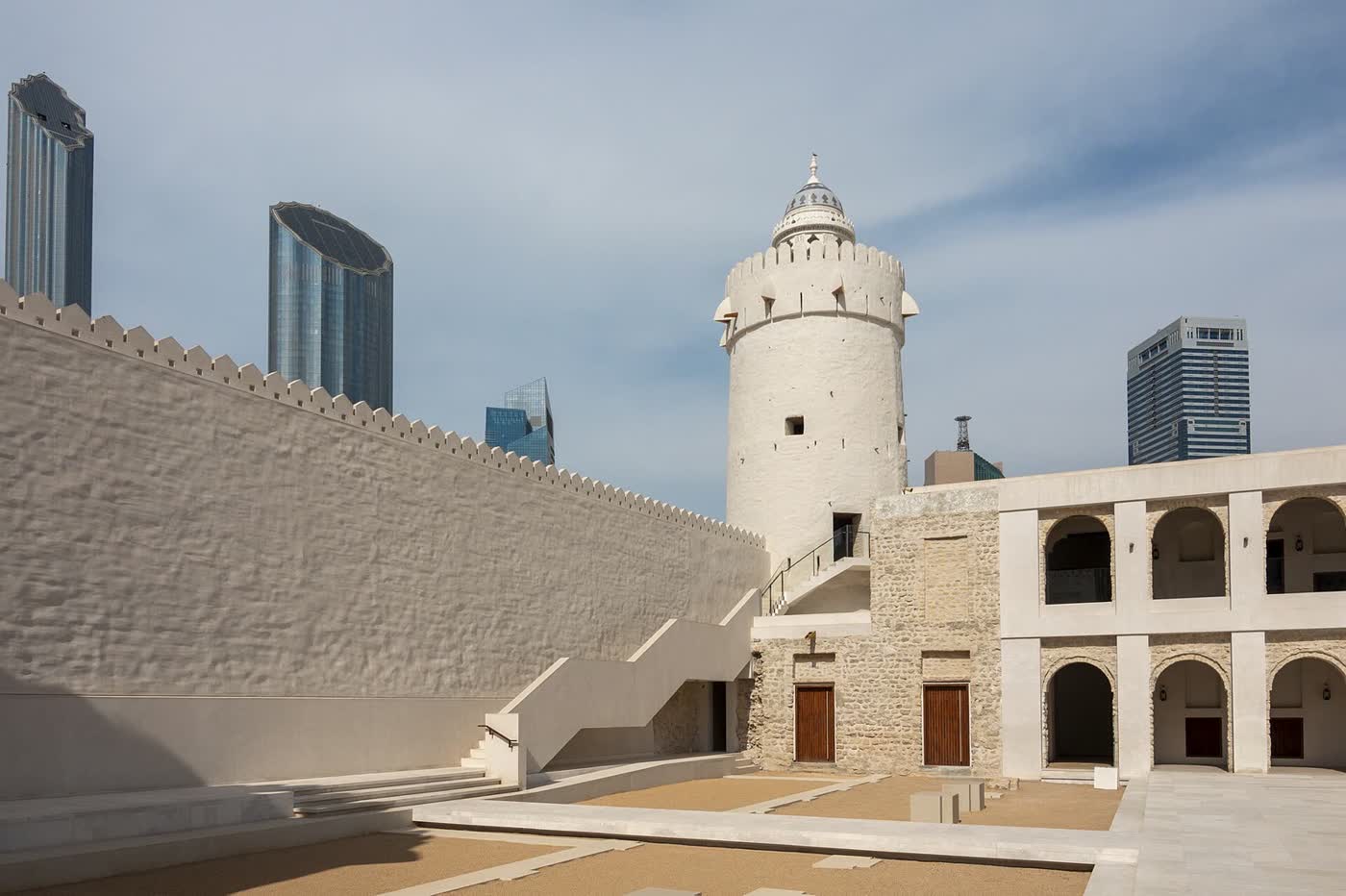 The white watchtower and arcaded courtyard of Qasr Al Hosn in Abu Dhabi, with glass towers behind