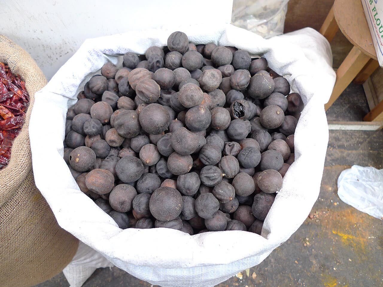 A white sack full of small, dark, wrinkled dried limes on sale at a market stall