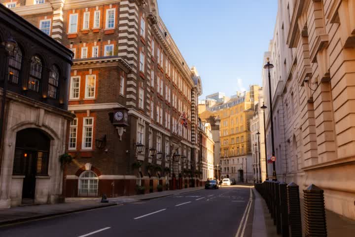 A quiet London street of red-brick and stone buildings in warm afternoon sun, with a Union flag on one facade