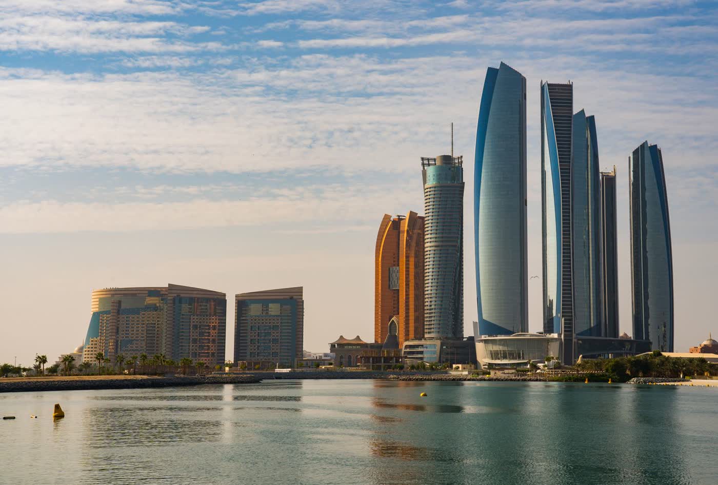 Abu Dhabi’s Etihad Towers and waterfront buildings reflected in calm water in soft morning light