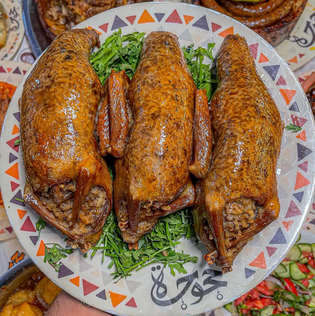 Three roasted stuffed pigeons on a bed of parsley, on a plate with a triangle-pattern rim