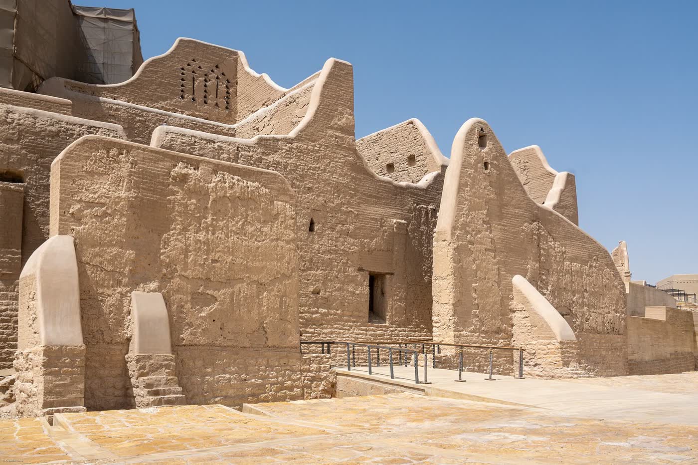 Sand-coloured mud-brick walls with rounded parapets and buttresses under a clear blue sky