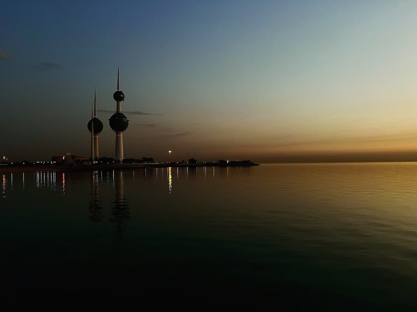 The two Kuwait Towers silhouetted against a dusk sky, reflected in calm sea water