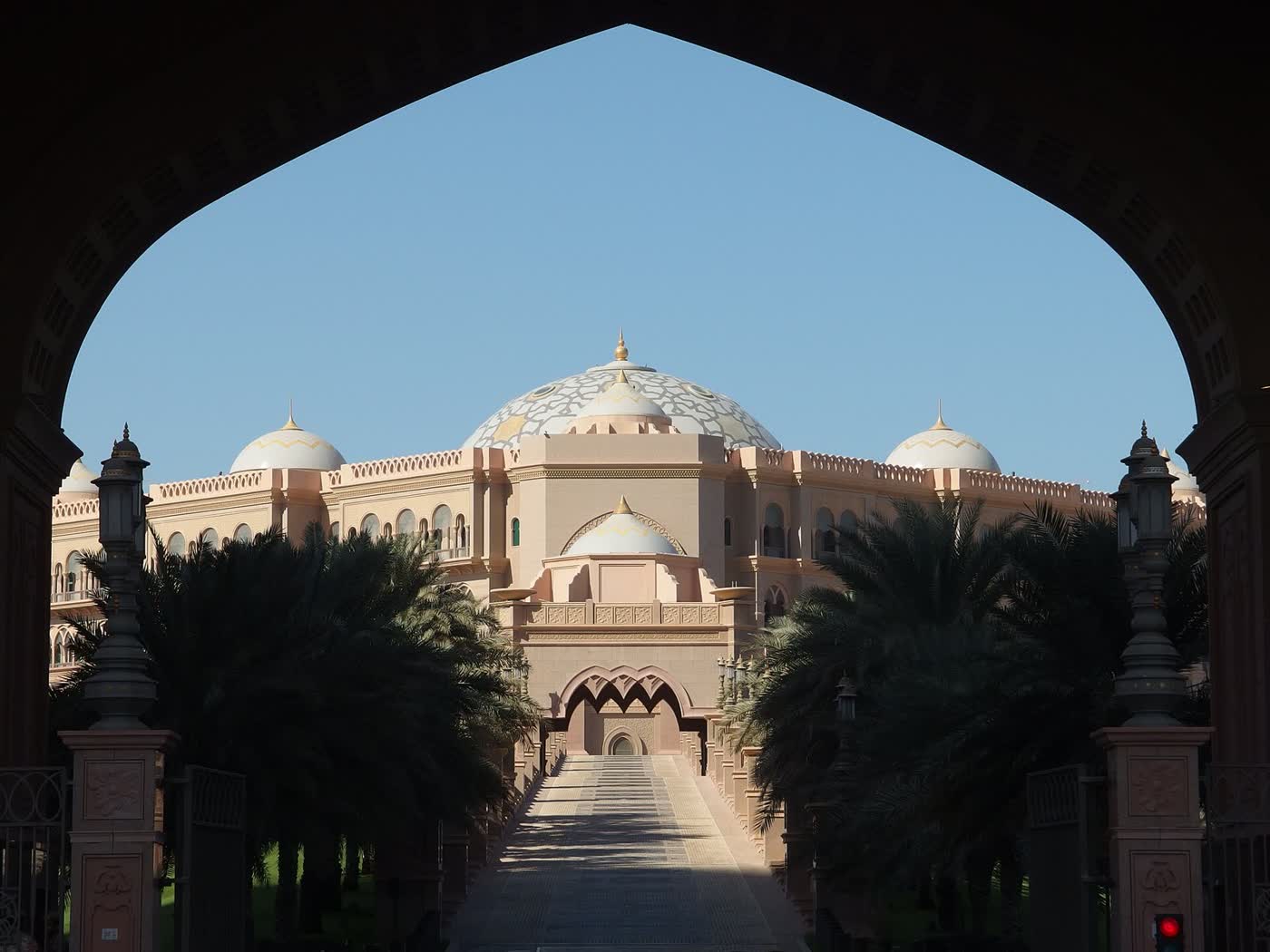 The pale domes of Emirates Palace in Abu Dhabi seen through a pointed arch framed by palm trees