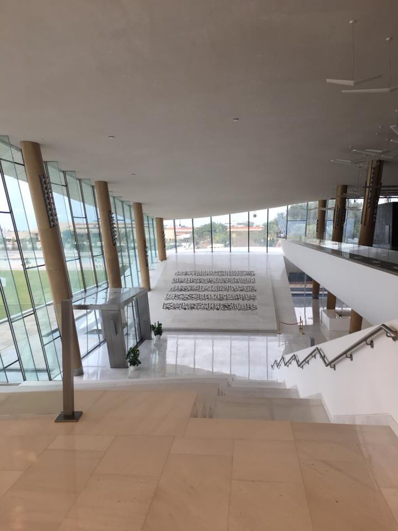 A bright atrium inside Etihad Museum with tall glass walls, pale timber columns and a large calligraphic floor panel