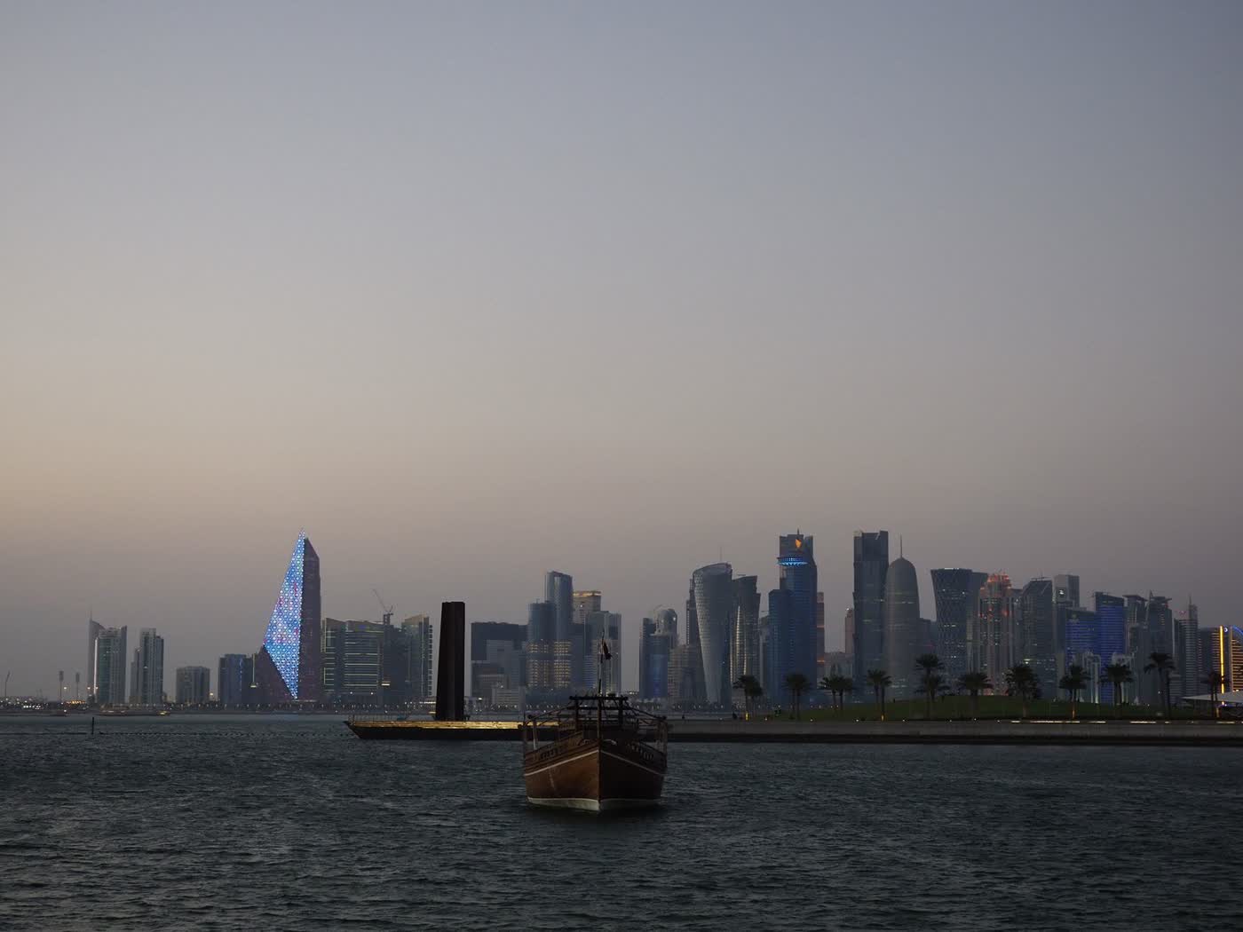 A traditional wooden dhow on the water at dusk with the Doha skyline behind it