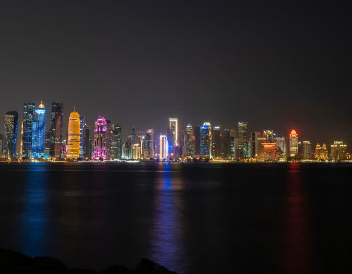 Illuminated skyscrapers of Doha’s West Bay skyline at night, reflected in dark water