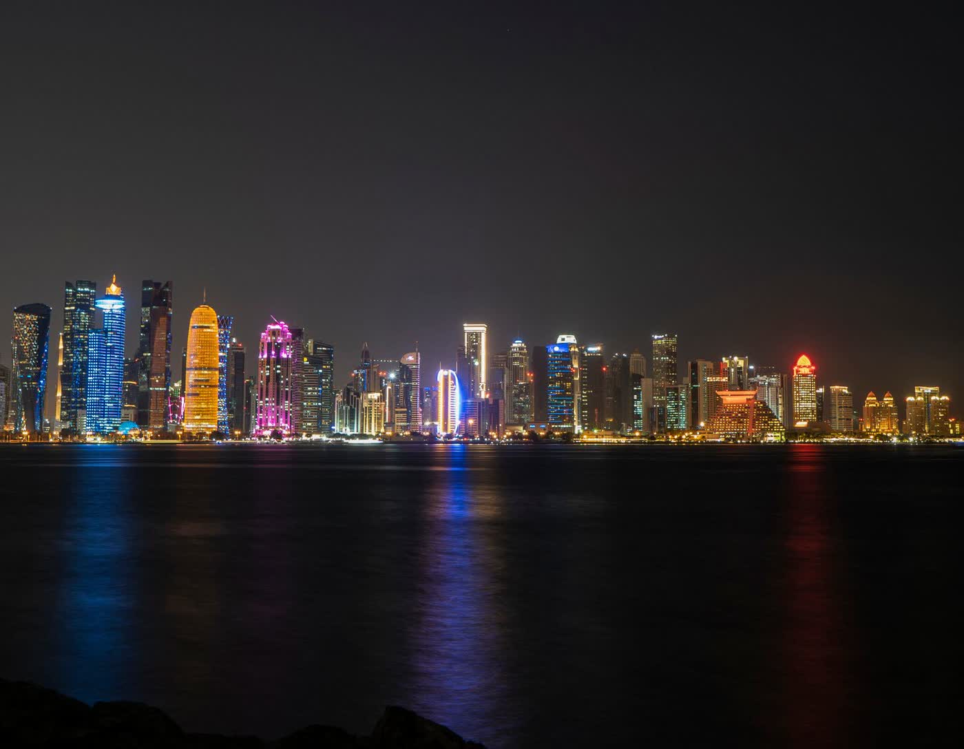 Illuminated skyscrapers of Doha’s West Bay skyline at night, reflected in dark water