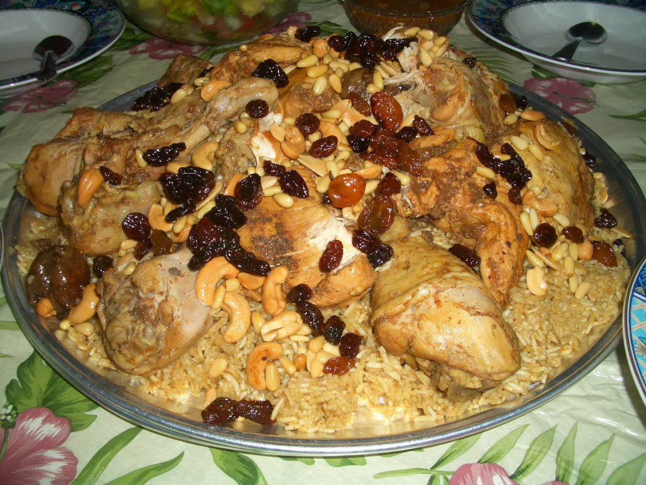 A platter of chicken kabsa on spiced rice, garnished with toasted nuts and raisins