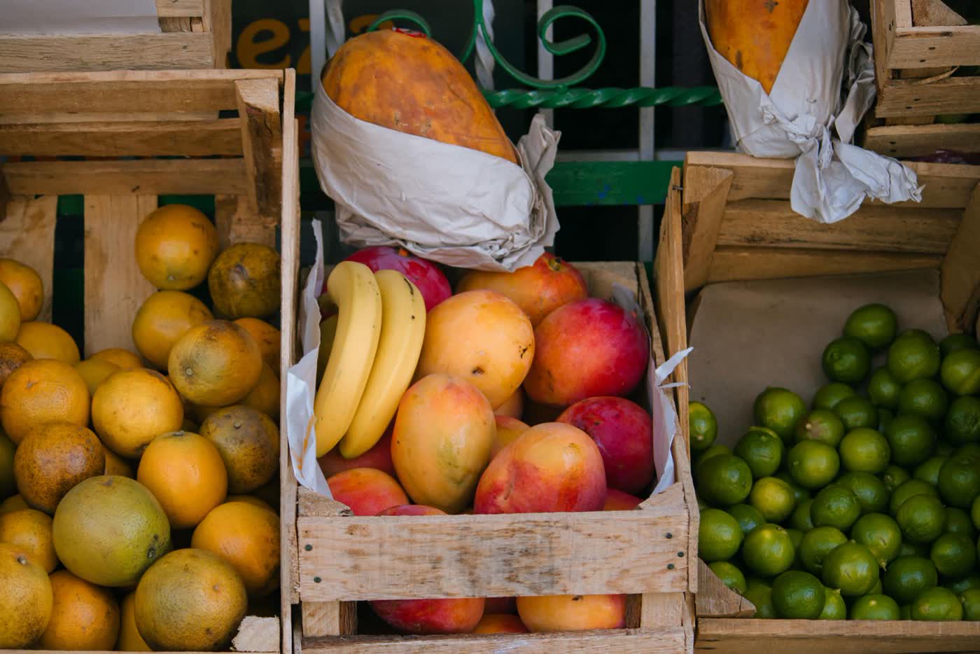 Wooden crates of oranges, mangoes, bananas and limes at a market stall